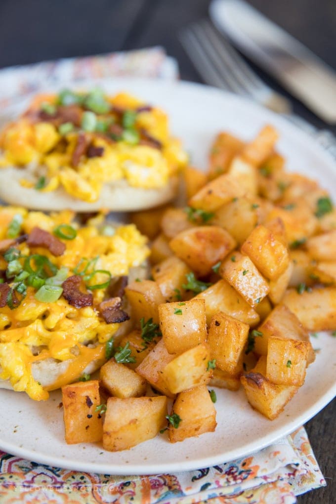 white plate, breakfast potatoes, english muffins with scrambled eggs and bacon