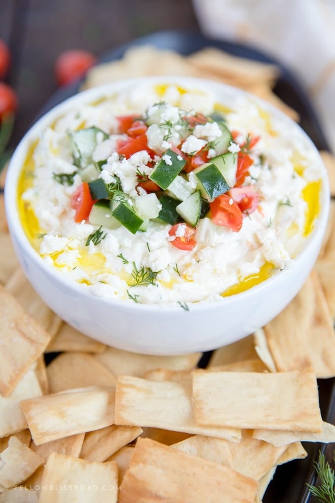 Greek Whipped Feta Cheese Dip in a bowl topped with cucumber and tomatoes and surrounded by pita chips