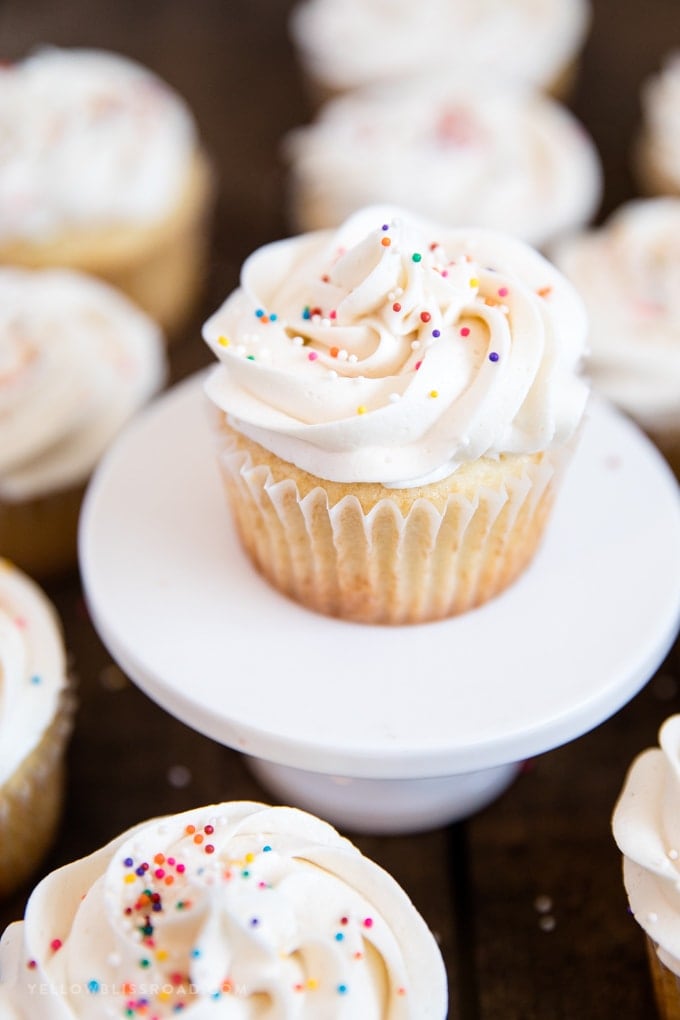 vanilla cupcake on a white plate surrounded by cupcakes