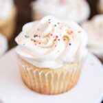 A close up of a vanilla cupcake on a plate, with vanilla frosting