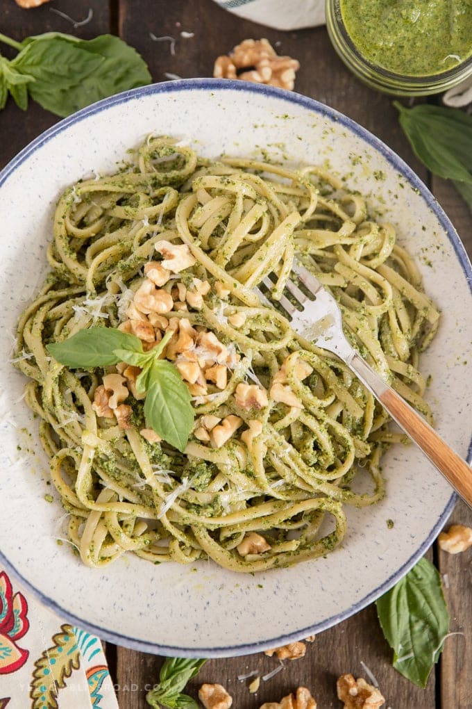 Homemade Walnut Basil Pesto recipe over pasta in a large bowl with a wooden fork.