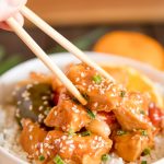 orange chicken, bell peppers, rice, sesame seeds, white bowl, chopsticks
