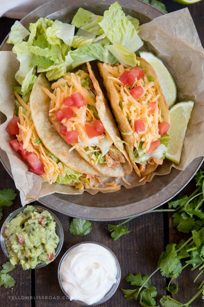 Aluminum pie plate holding three chicken tacos, with guacamole and sour cream and cilantro