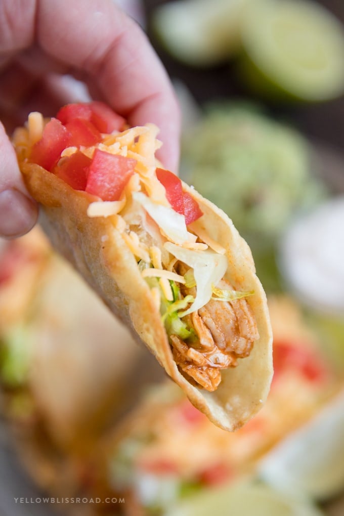 a hand holding a hard shell taco with shredded chicken, lettuce, cheese and tomatoes.