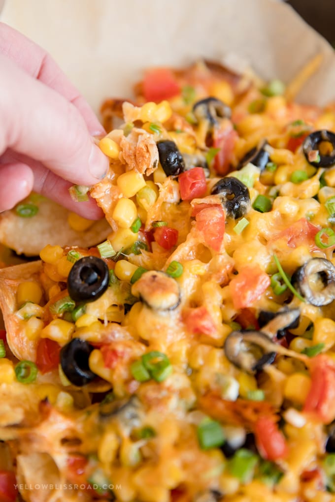 a hand grabbing a chip from these Loaded chicken nachos