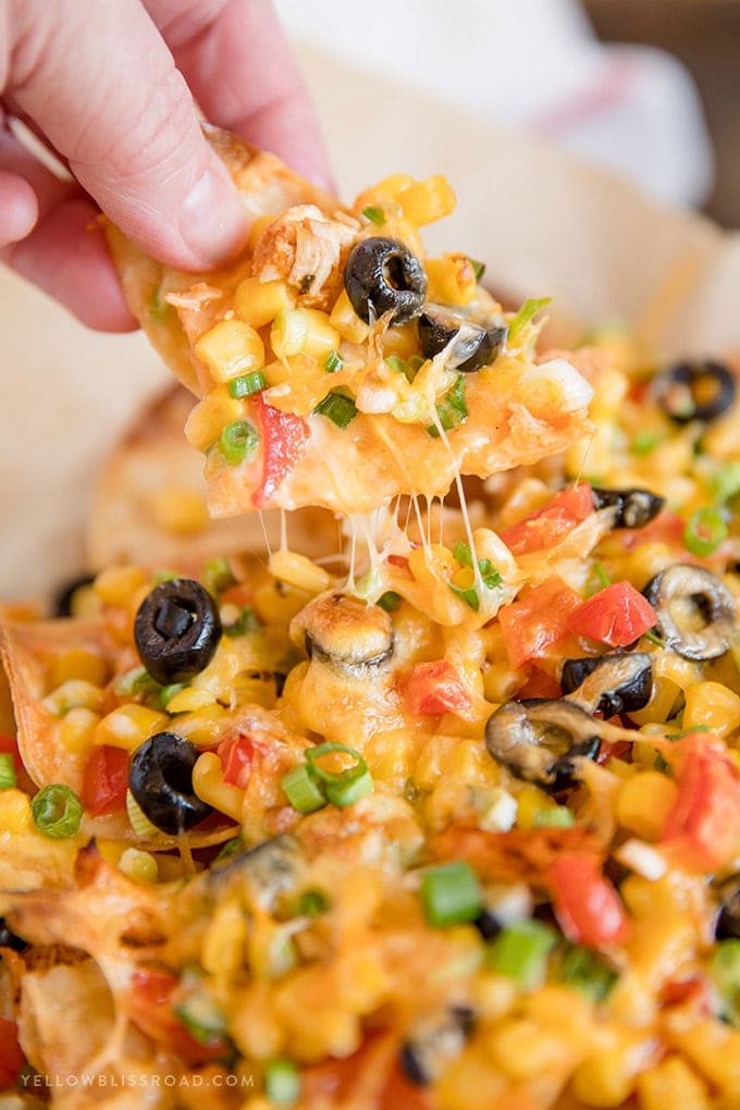 A hand grabbing a chip from a plate of loaded chicken nachos