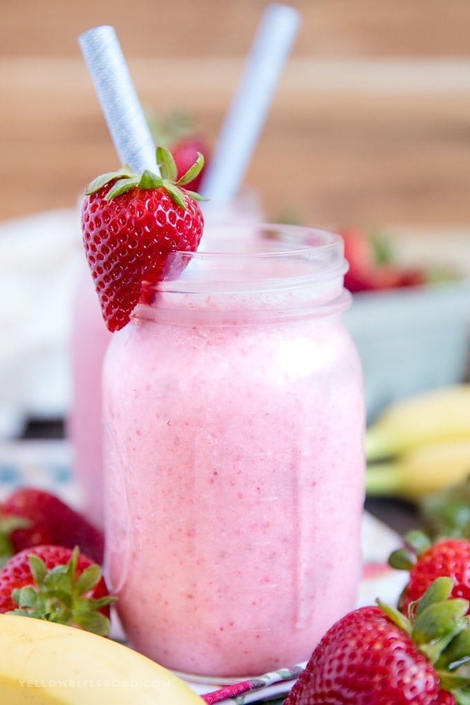 Strawberry banana smoothie in a mason jar with a strawberry garnish and paper straw