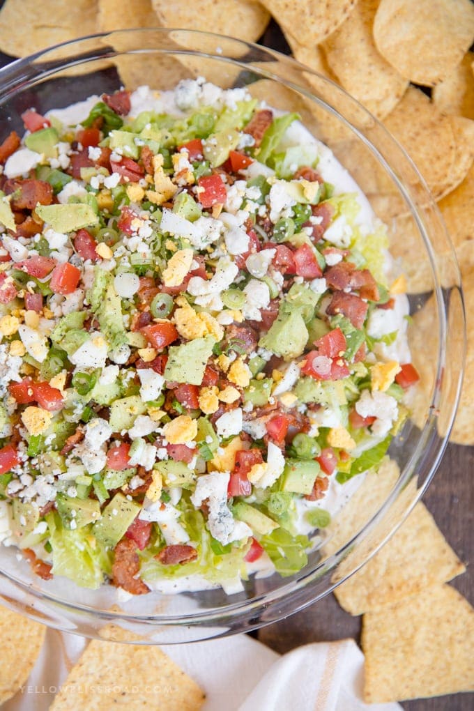 a delicious cobb salad dip in a clear dish surrounded by tortilla chips