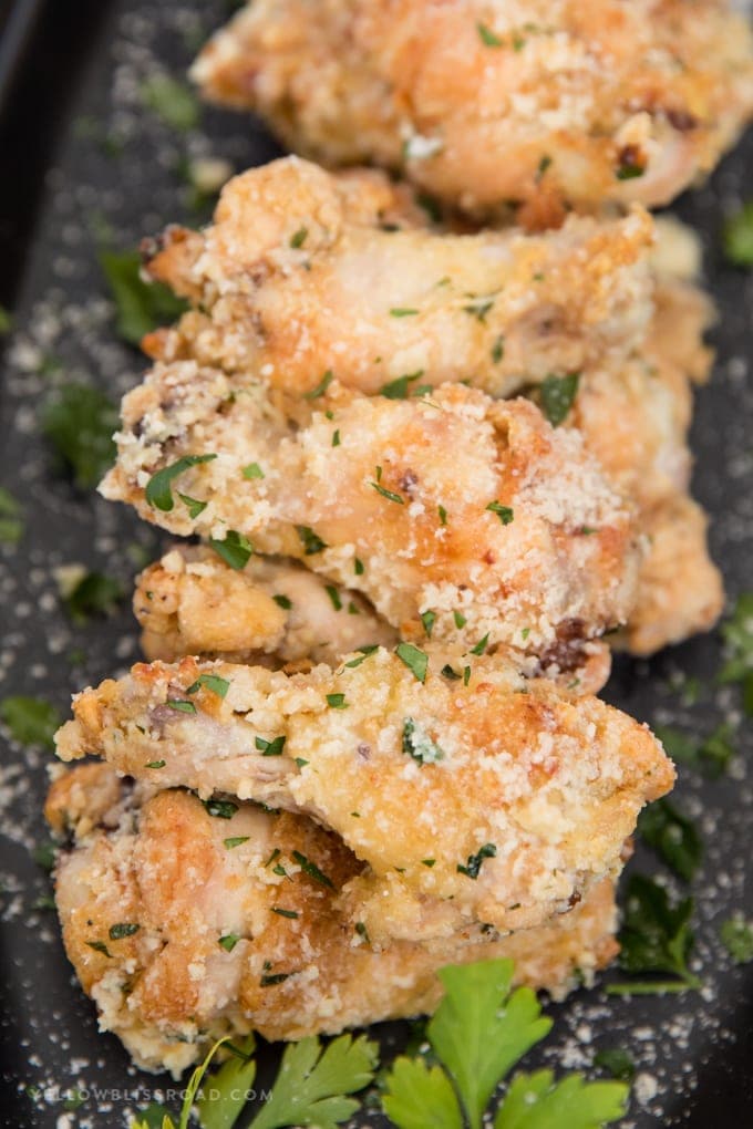 Crispy Baked Garlic Parmesan Chicken Wings in garlic parmesan sauce stacked together on a platter with parsley