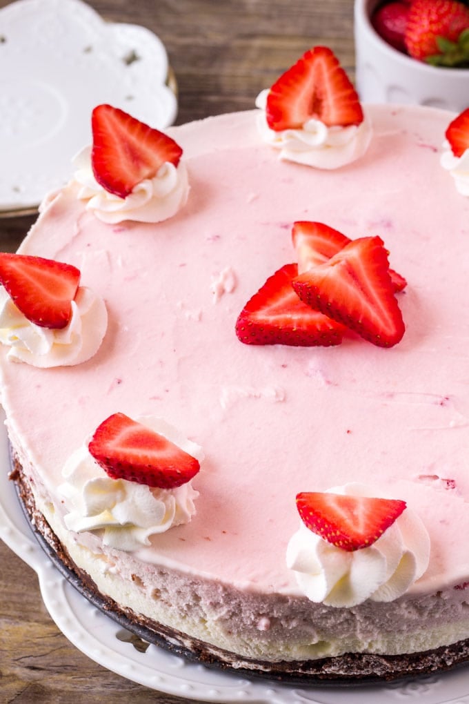 Homemade ice cream cake with a brownie bottom, layers of vanilla and strawberry ice cream, then topped with whipped cream and berries. 