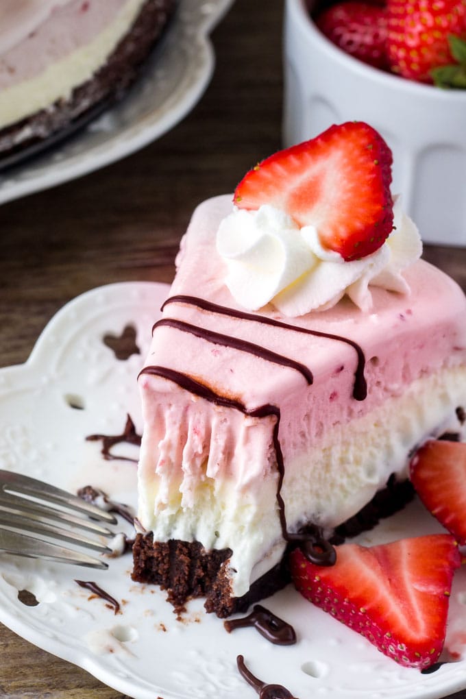 A slice of neapolitan ice cream cake with a layer of brownie, vanilla ice cream, then strawberry ice cream. 