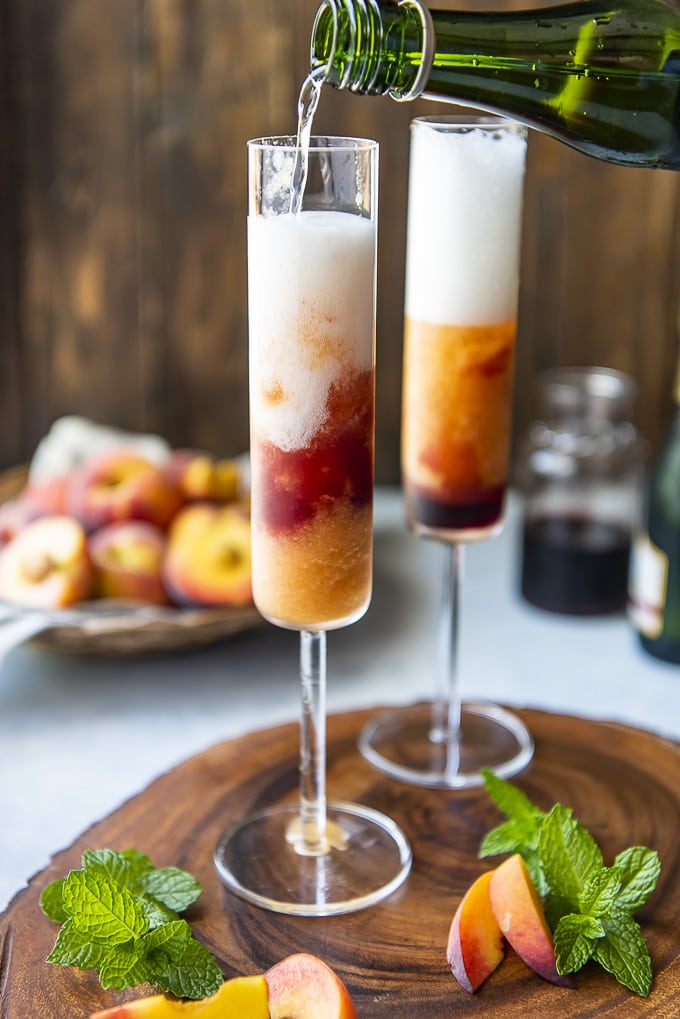 No need to wait for peach season - you can enjoy a Frozen Peach Bellini any time of the year! This easy 4-ingredient brunch cocktail is made with frozen peaches, peach vodka, and a kiss of grenadine for an extra kick of booze. Champagne being poured into frozen peach bellinis