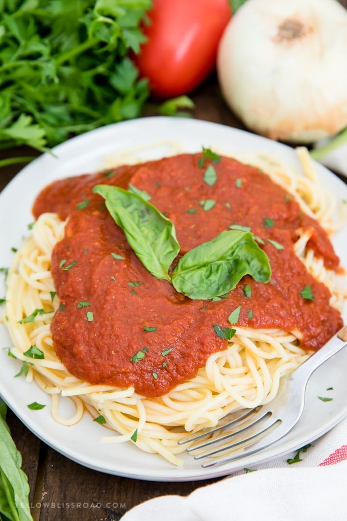 Easy Homemade Spaghetti Sauce - Simple to make and so much better than jarred. Make a double or triple batch to freeze for later so you're always ready for spaghetti night! Easy Homemade Spaghetti Sauce over spaghetti with basil leaves