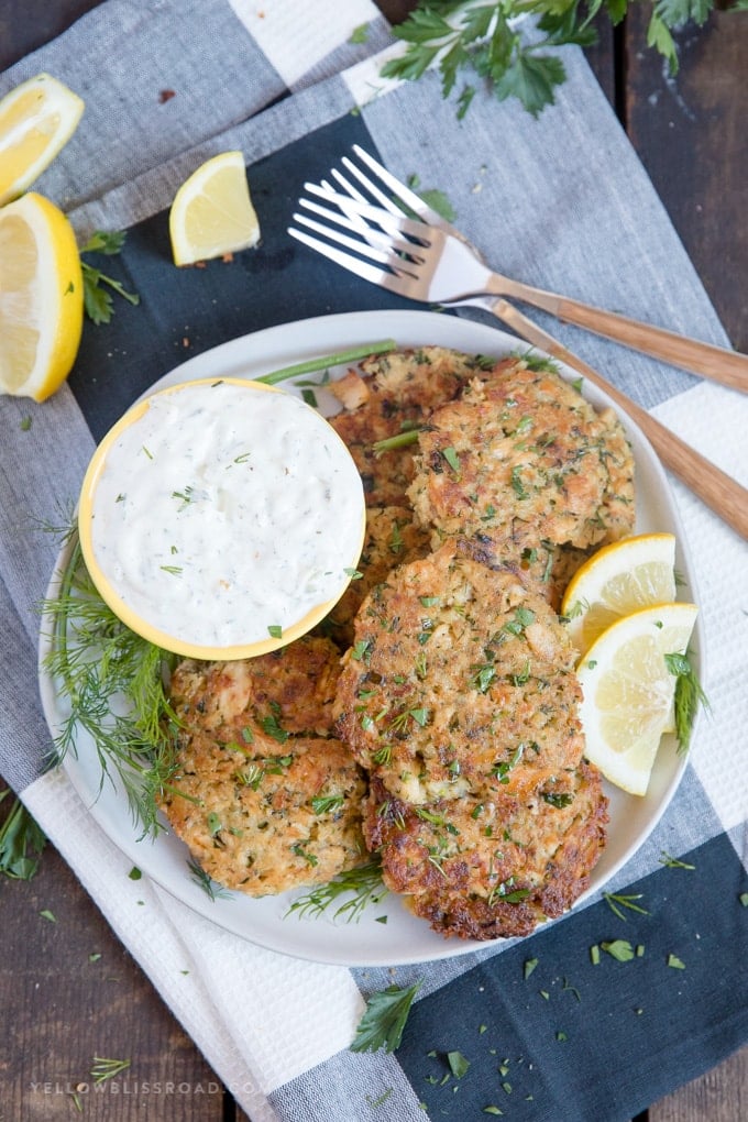 salmon patties on a plate with homemade tartar sauce and lemon wedges sitting on a black and white towel | salmon patty recipe | salmon cakes