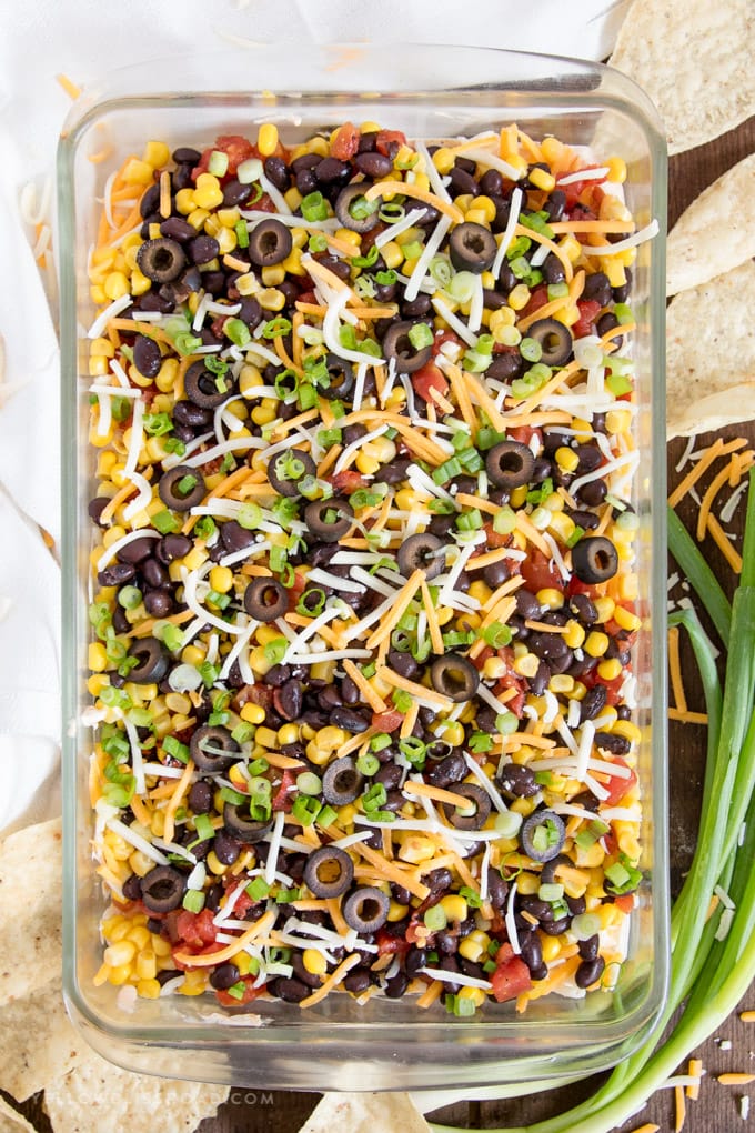 Southwestern 7 Layer Dip - Layers of kicked up tomatoes, black beans and corn on top of a spicy, cream cheese base. This is the appetizer you'll want to bring to every party! southwest 7 layer dip overhead photo with tortilla chips and green onions