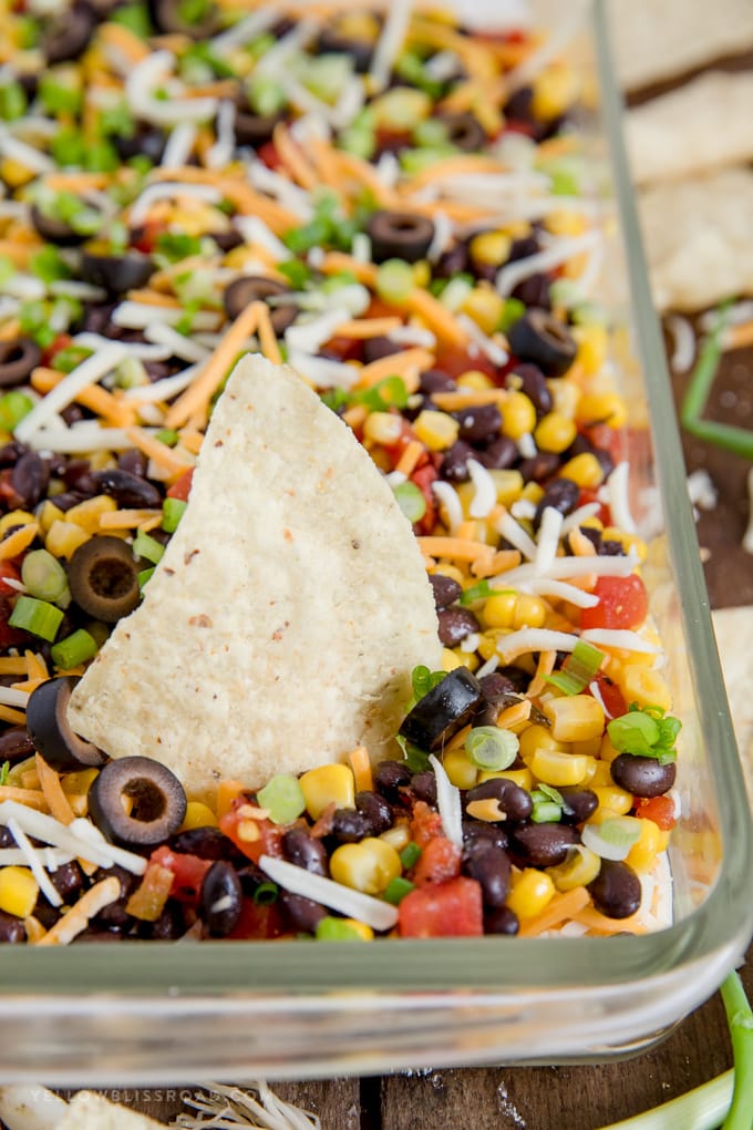 Southwestern 7 Layer Dip - Layers of kicked up tomatoes, black beans and corn on top of a spicy, cream cheese base. This is the appetizer you'll want to bring to every party! southwest 7 layer dip with a tortilla chip stuck in it