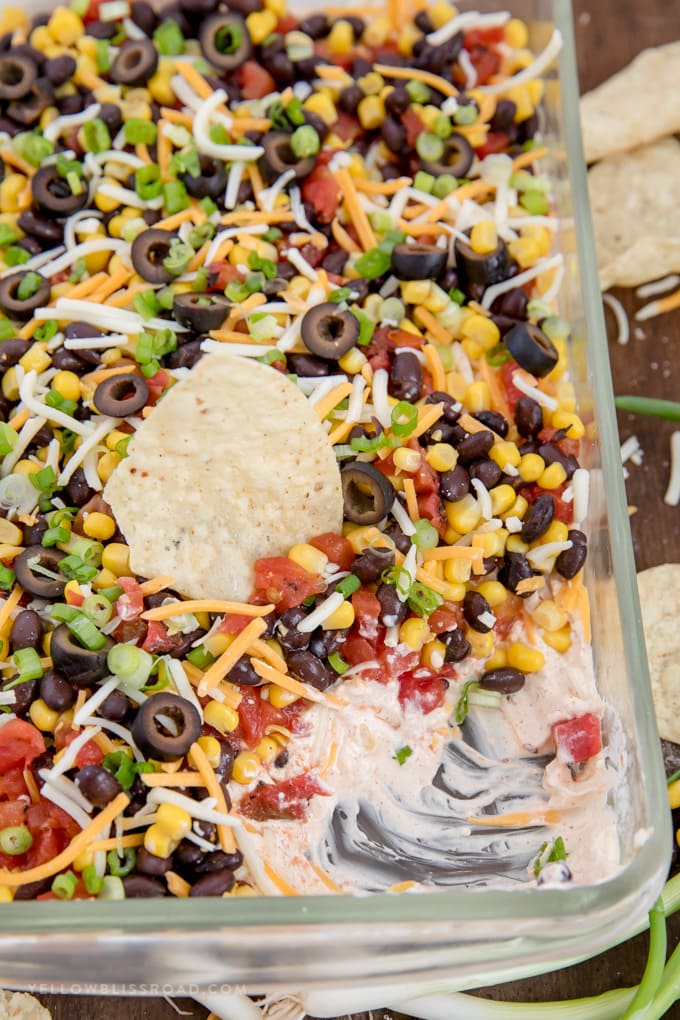 Southwestern 7 Layer Dip - Layers of kicked up tomatoes, black beans and corn on top of a spicy, cream cheese base. This is the appetizer you'll want to bring to every party! half eaten southwest 7 layer dip