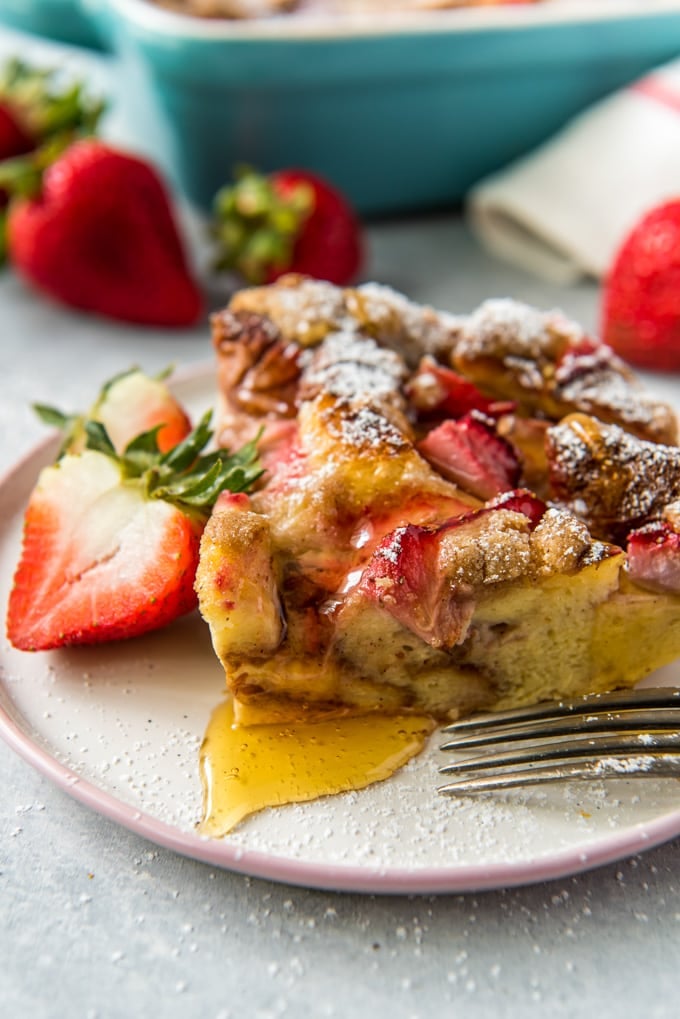 A piece of strawberry baked french toast with syrup on a white plate and topped with syrup and powdered sugar.