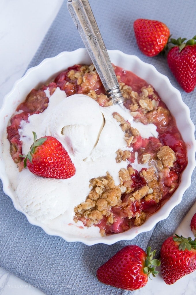 A serving of Strawberry Rhubarb Crisp with vanilla ice cream and a strawberry on top