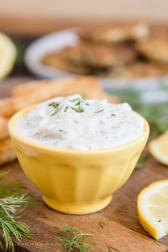 homemade tartar sauce recipe - sauce in a yellow cup with lemon wedges near by