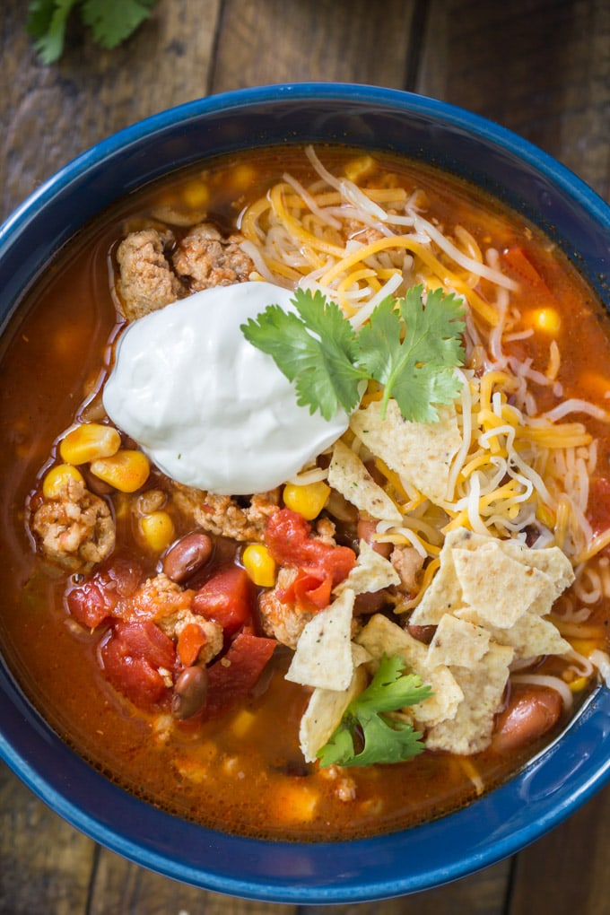 a bowl of taco soup with sour cream, tortilla chips and cilantro on top