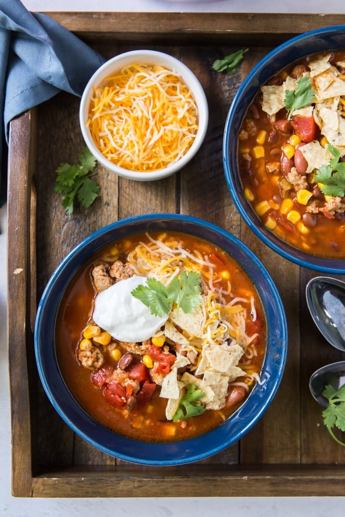 A bowl filled taco soup and side dish of shredded cheese.