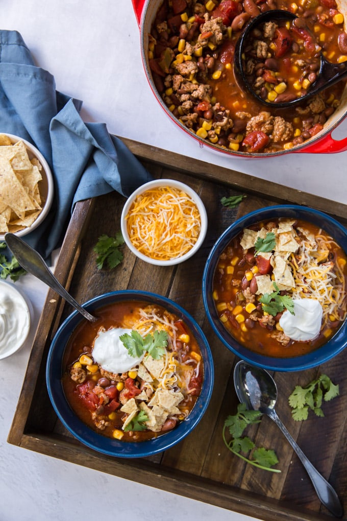 A bowl filled taco soup and side dish of shredded cheese.