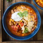 A bowl of taco soup, topped with cheese, sour cream, and chips.