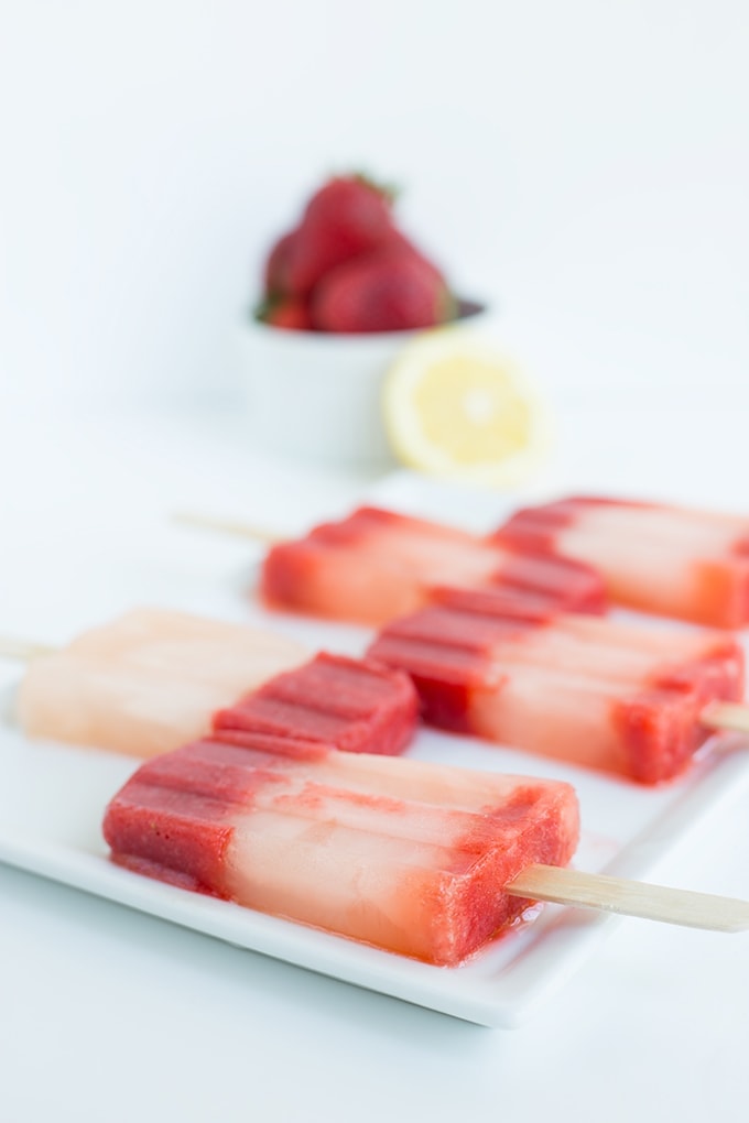 strawberry lemonade popsicles on a plate with strawberries and lemons