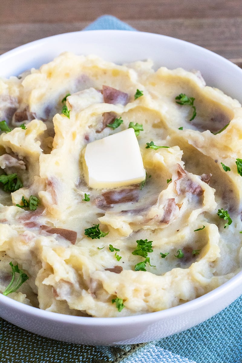 Garlic mashed potatoes in a serving bowl garnished with chopped parsley and a pat of butter