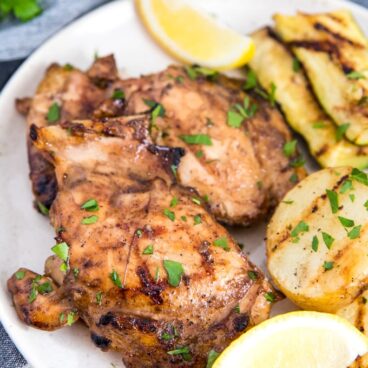 Grilled chicken thighs on a plate with parsley and lemon wedges.