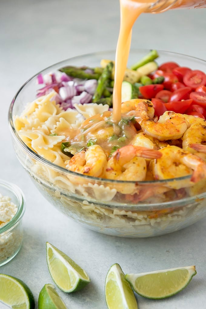 dressing being poured onto Grilled Shrimp Pasta Salad before tossing