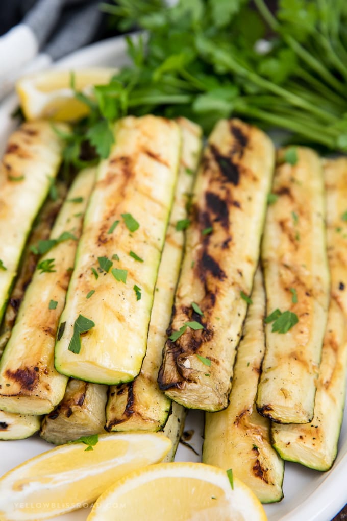 Grilled Zucchini, marinated in lemon juice and olive oil, is a healthy summer side dish that everyone loves! grilled zucchini strips on a plate with lemon.