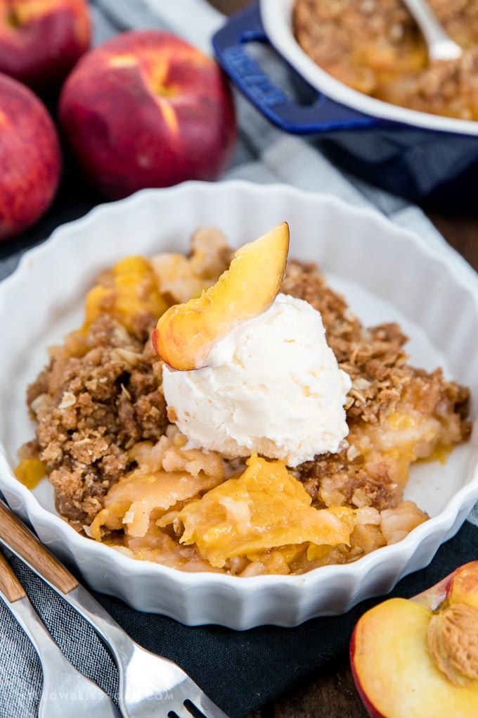 Fresh peach crisp in a dish with a scoop of vanilla ice cream.