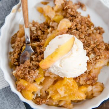 Peach crisp with oat topping and a scoop of vanilla ice cream.