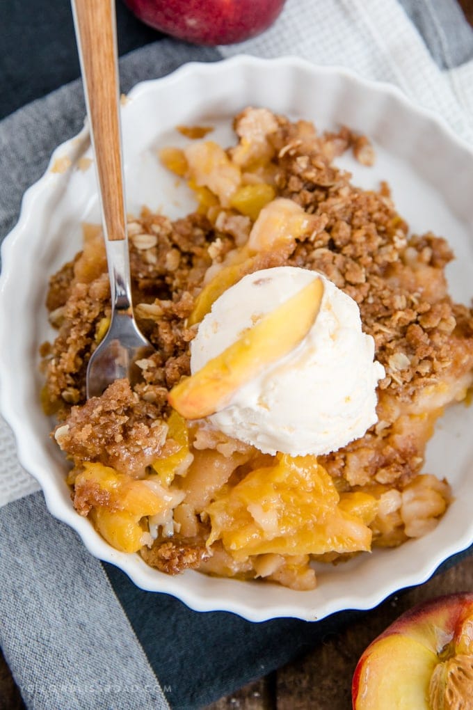 Peach crisp with oat topping and a scoop of vanilla ice cream.