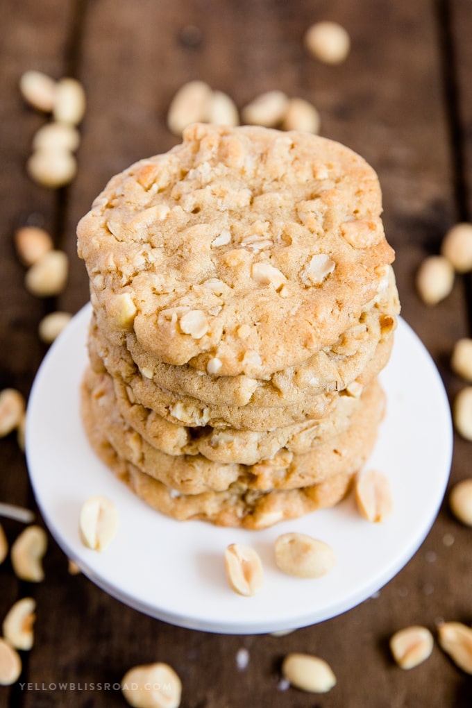 A stack of oatmeal peanut butter cookies on a small white plate with a wood background and peanuts scattered.