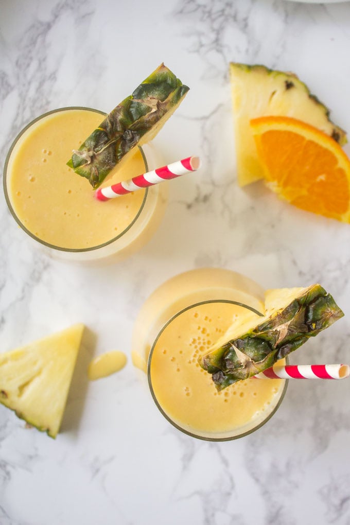 overhead shot of pineapple smoothies in glasses with pineapple and orange slices in the background