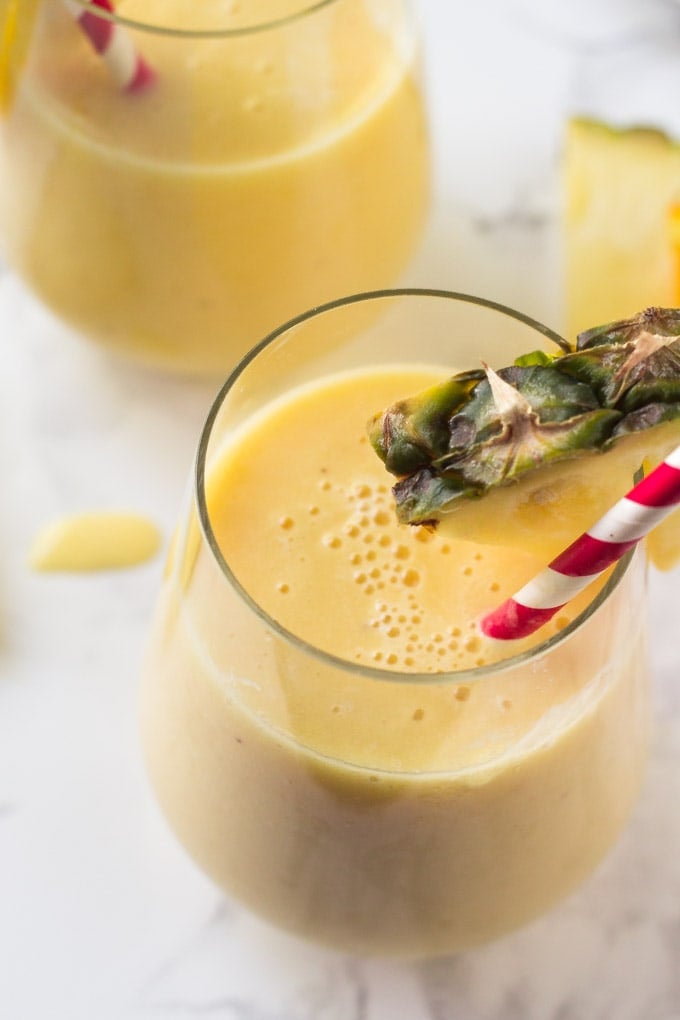 pineapple smoothie in a glass with a straw and pineapple wedge