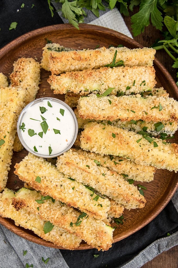 zucchini fries arranged on a wood plate with a cup of ranch dressing.