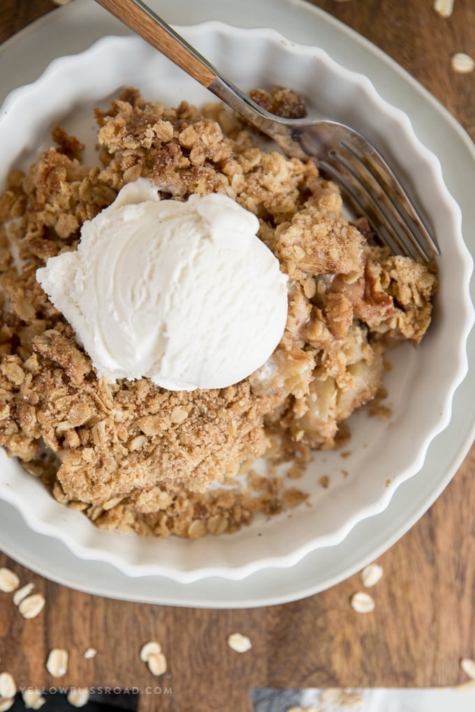 Apple crumble in a white dish with vanilla ice cream and a fork