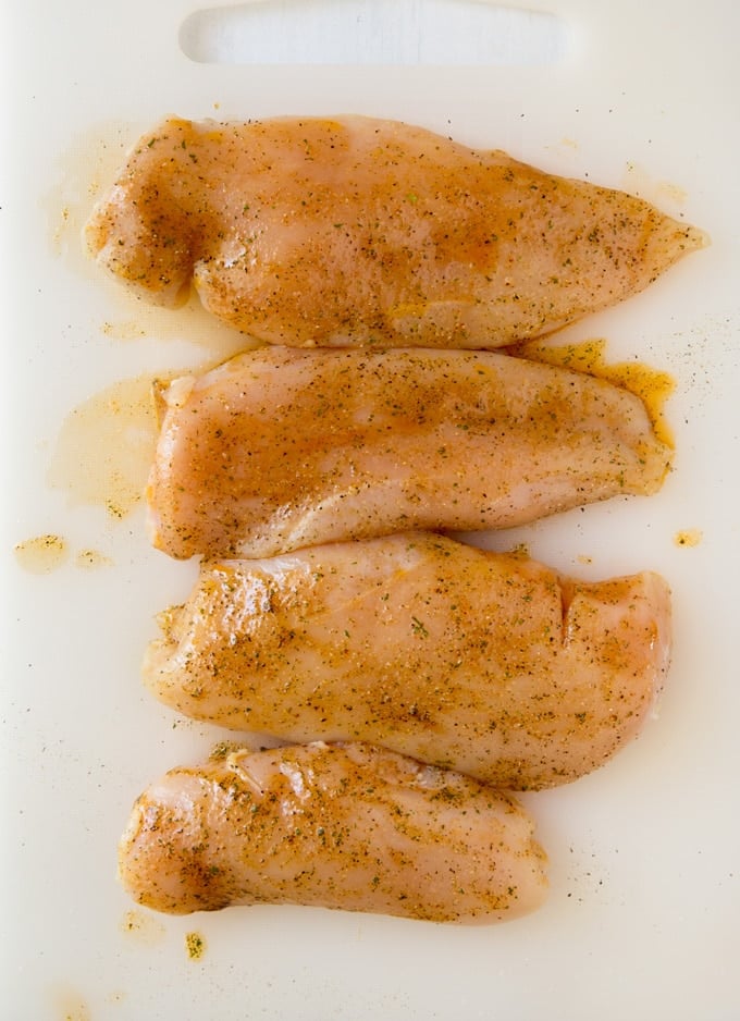 Raw seasoned chicken breasts on a white cutting board.