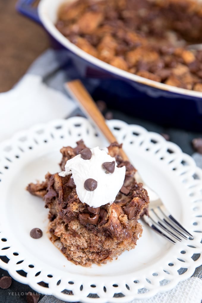 a serving chocolate bread pudding on a white plate topped with whipped bream. 