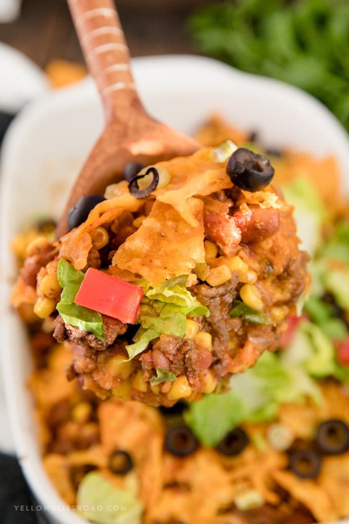 A scoop of Dorito Taco Salad Casserole on a wooden spoon.