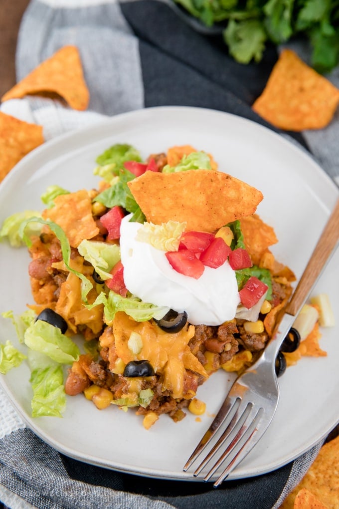 A serving of Dorito Taco Casserole on a plate with lettuce, tomatoes and sour cream