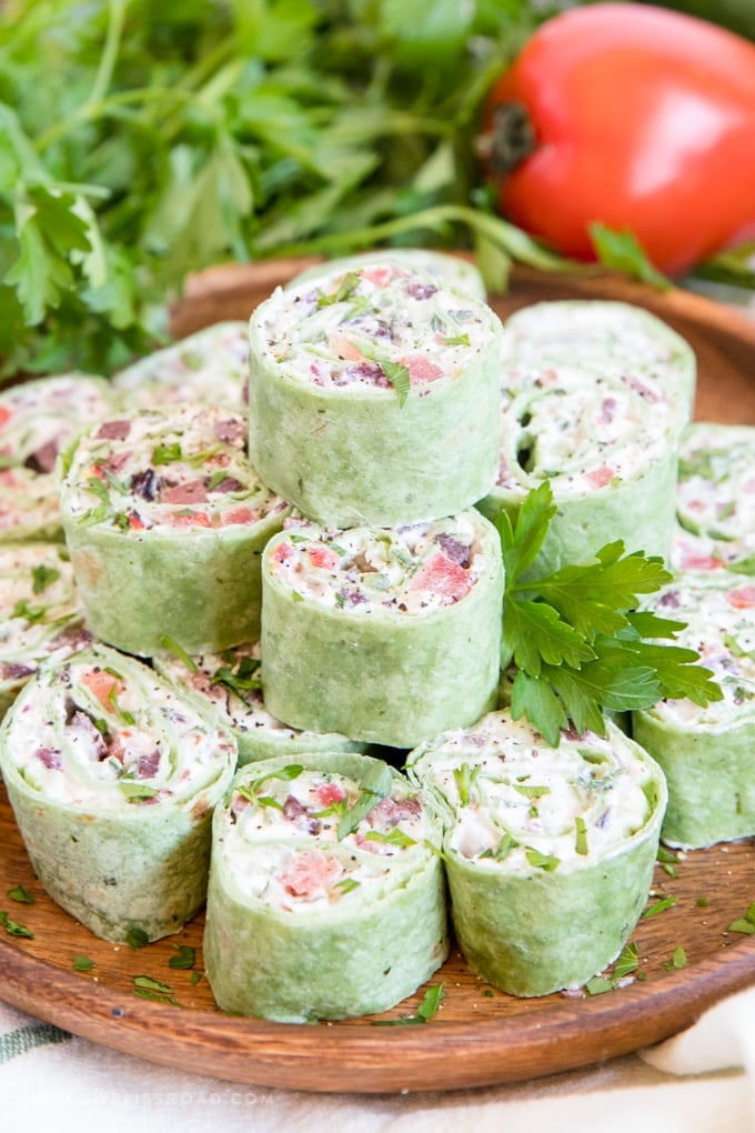 Creamy Greek Salad Pinwheels appetizer stacked on a wood plate.