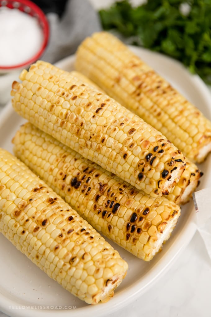 Grilled corn on the cob, stacked on a white plate.