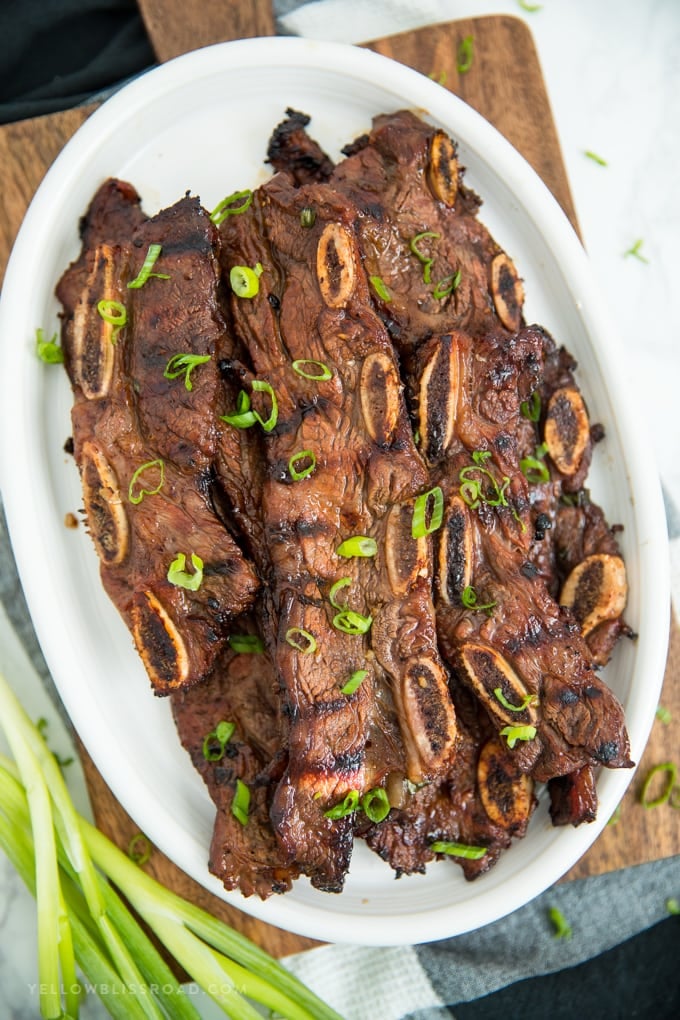 A white platter full of grilled Korean short ribs with green onions