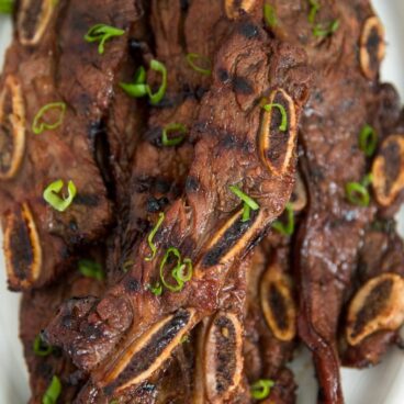 korean short ribs grilled and sitting on a white platter with sliced green onions.