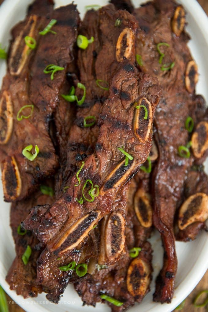 korean short ribs grilled and sitting on a white platter with sliced green onions. 